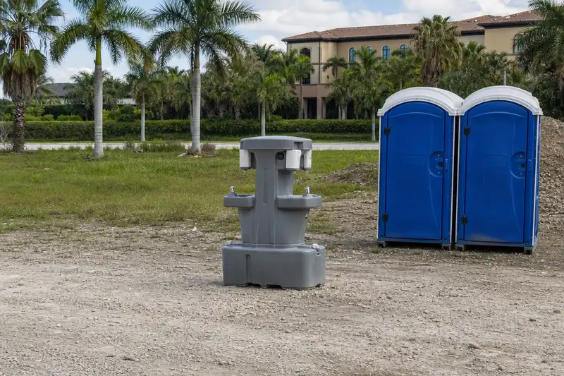 Free-standing two-sided handwash station beside blue portable toilets